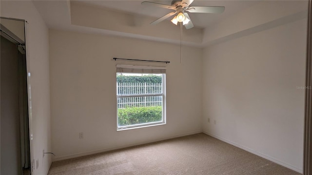 carpeted empty room featuring a raised ceiling and ceiling fan