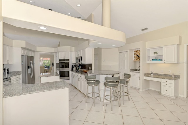 kitchen with white cabinets, a kitchen island, light stone counters, and appliances with stainless steel finishes