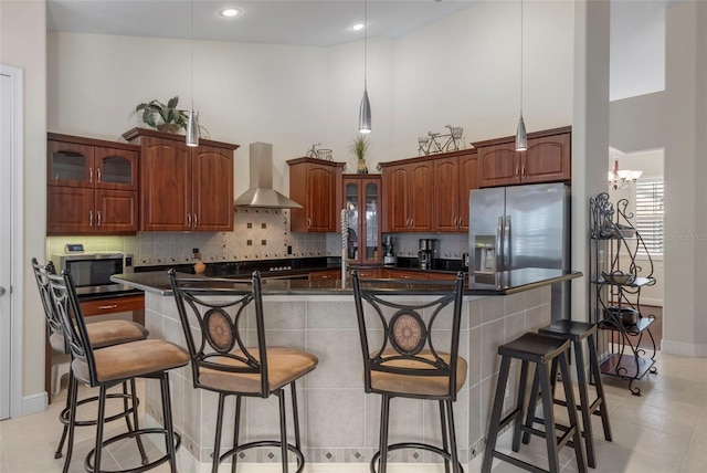 kitchen with a kitchen bar, a high ceiling, a kitchen island with sink, stainless steel appliances, and wall chimney range hood