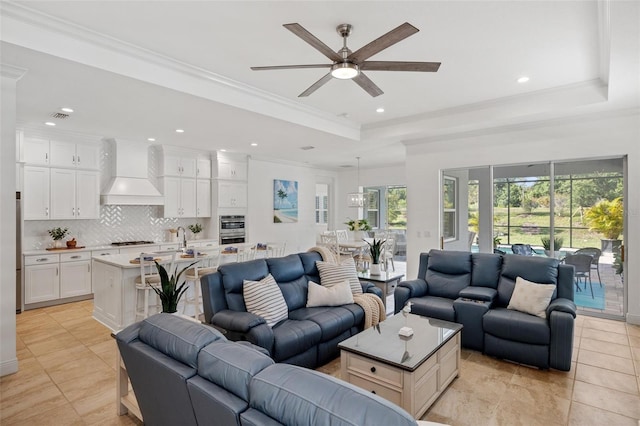 tiled living room with a tray ceiling, ceiling fan, and crown molding