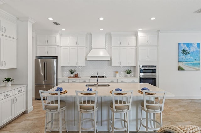 kitchen featuring custom exhaust hood, a kitchen island with sink, white cabinets, sink, and stainless steel appliances