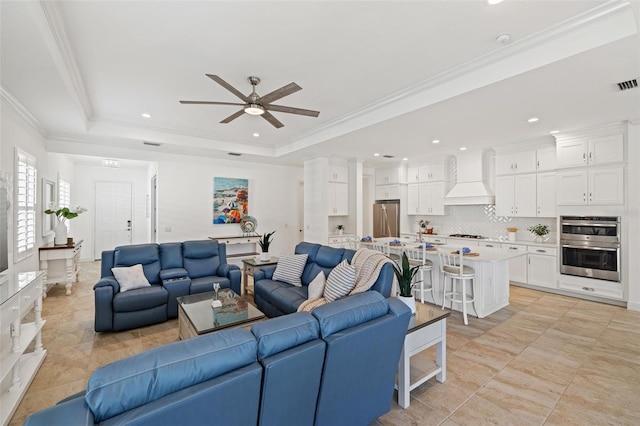 tiled living room with a raised ceiling, ceiling fan, and crown molding