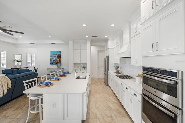 kitchen with appliances with stainless steel finishes, a breakfast bar, custom range hood, a spacious island, and sink