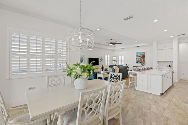 dining space with ceiling fan with notable chandelier, a tray ceiling, crown molding, and sink