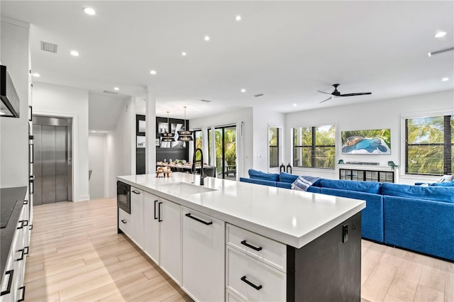 kitchen featuring a center island with sink, ceiling fan with notable chandelier, white cabinets, sink, and built in microwave