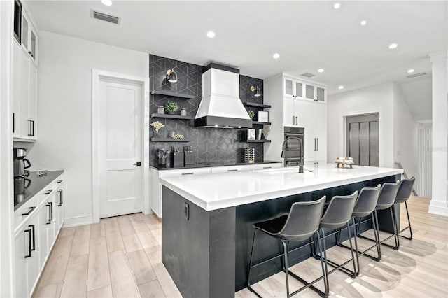 kitchen featuring a breakfast bar, a spacious island, custom range hood, tasteful backsplash, and white cabinetry