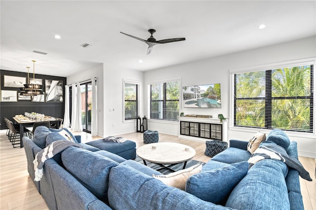 living room with ceiling fan with notable chandelier, light hardwood / wood-style floors, and plenty of natural light