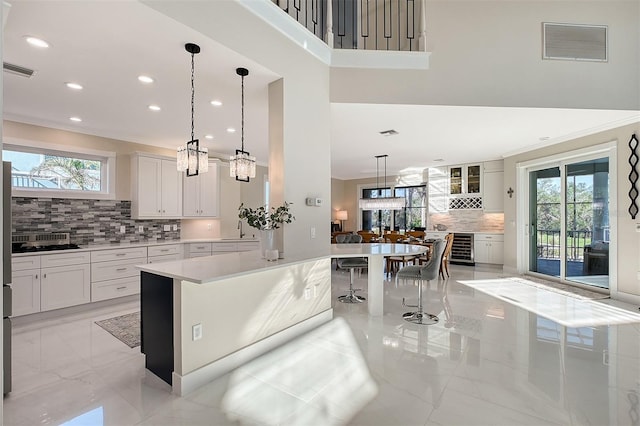 kitchen with a breakfast bar, white cabinets, hanging light fixtures, wine cooler, and decorative backsplash