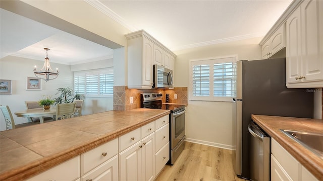 kitchen featuring hanging light fixtures, light hardwood / wood-style flooring, tile counters, stainless steel appliances, and a chandelier