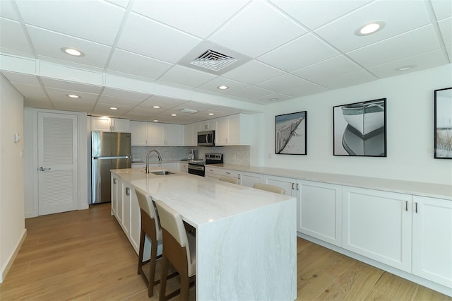 kitchen with light stone countertops, stainless steel appliances, sink, white cabinets, and an island with sink