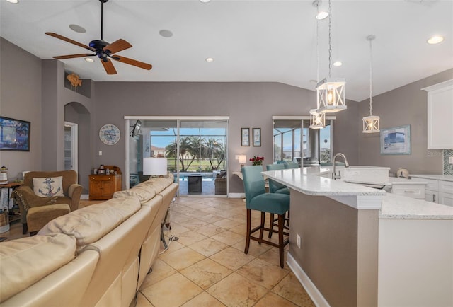 kitchen featuring a kitchen bar, a kitchen island with sink, ceiling fan, pendant lighting, and white cabinets