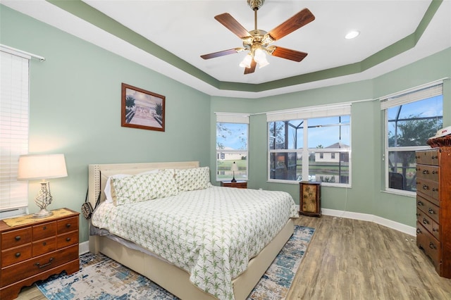 bedroom featuring multiple windows, wood-type flooring, a tray ceiling, and ceiling fan