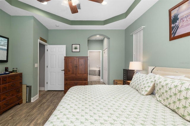 bedroom with connected bathroom, a raised ceiling, ceiling fan, and dark wood-type flooring