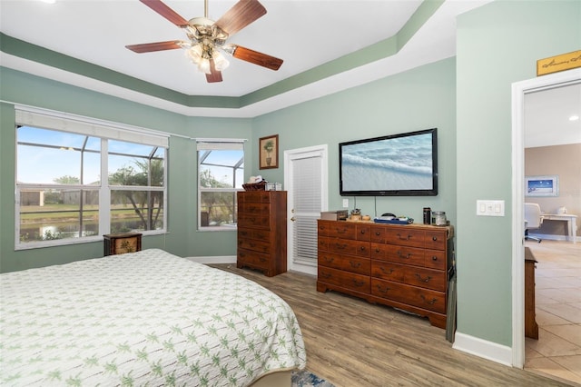 bedroom with a tray ceiling, ceiling fan, a water view, and wood-type flooring