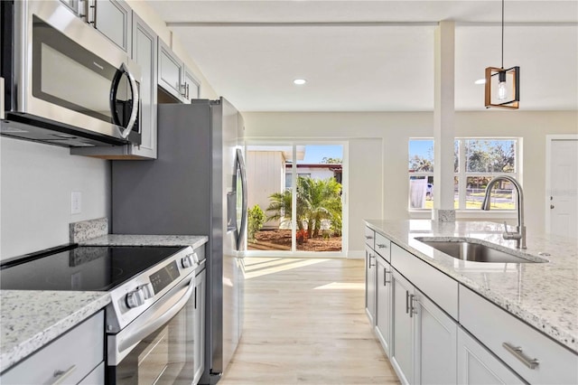 kitchen with sink, light stone counters, pendant lighting, appliances with stainless steel finishes, and light wood-type flooring