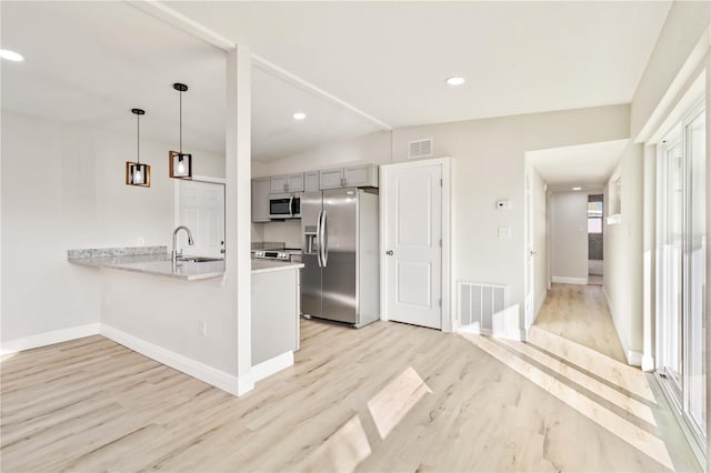 kitchen featuring kitchen peninsula, stainless steel appliances, sink, light hardwood / wood-style floors, and hanging light fixtures