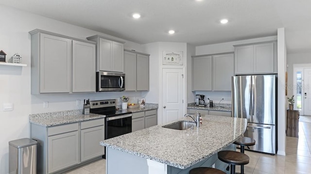 kitchen featuring appliances with stainless steel finishes, a breakfast bar, an island with sink, sink, and light stone countertops