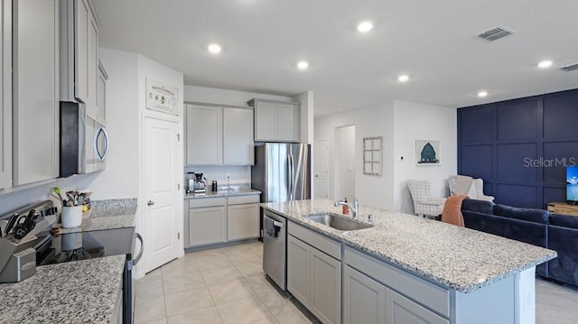 kitchen with sink, light tile patterned floors, appliances with stainless steel finishes, gray cabinetry, and an island with sink