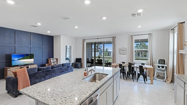 kitchen featuring sink, light tile patterned floors, stainless steel dishwasher, light stone countertops, and a kitchen island with sink