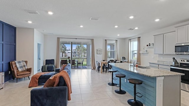 kitchen featuring a kitchen bar, sink, light stone counters, an island with sink, and stainless steel appliances