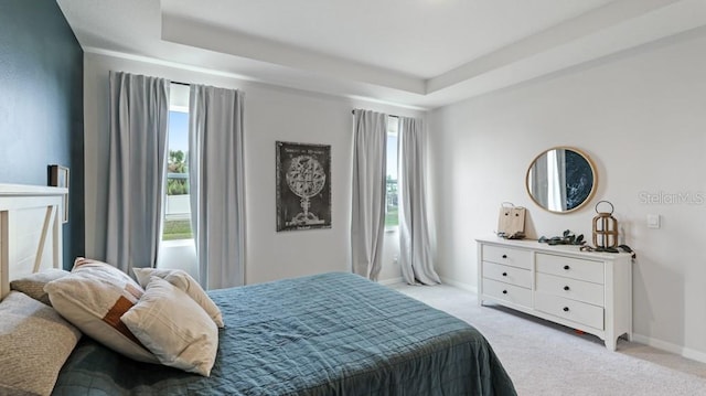 bedroom featuring a raised ceiling, light carpet, and multiple windows