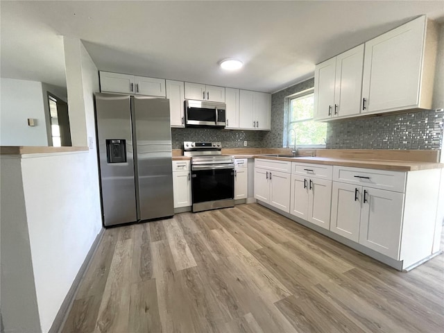 kitchen with sink, stainless steel appliances, backsplash, white cabinets, and light wood-type flooring