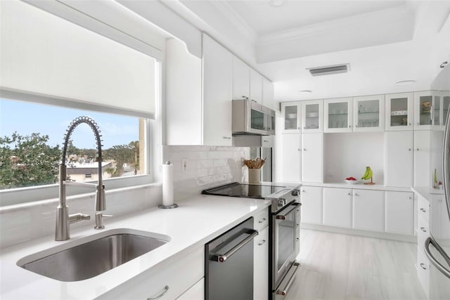 kitchen with appliances with stainless steel finishes, tasteful backsplash, white cabinetry, sink, and crown molding