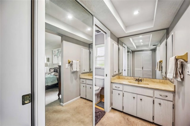 bathroom with toilet, vanity, and a raised ceiling