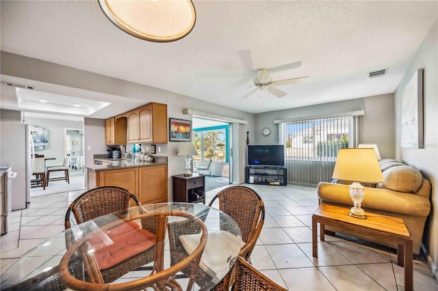 tiled dining space featuring a textured ceiling, a tray ceiling, and ceiling fan