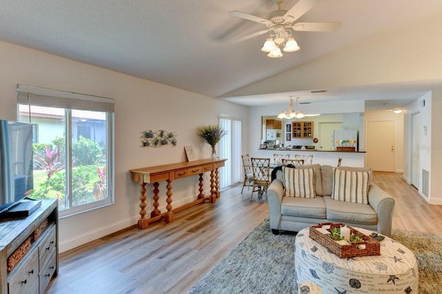 living room featuring ceiling fan with notable chandelier, light hardwood / wood-style floors, and vaulted ceiling