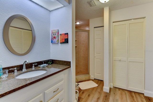 bathroom featuring vanity, a shower with shower door, wood-type flooring, and a textured ceiling