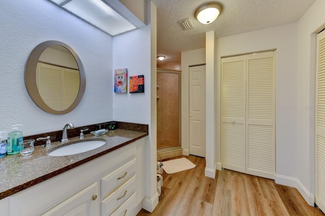 bathroom with an enclosed shower, vanity, wood-type flooring, and a textured ceiling