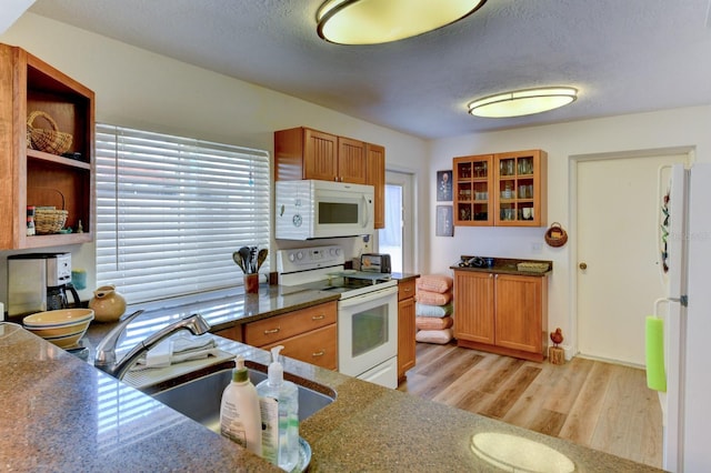 kitchen with sink, dark stone countertops, light hardwood / wood-style floors, a textured ceiling, and white appliances