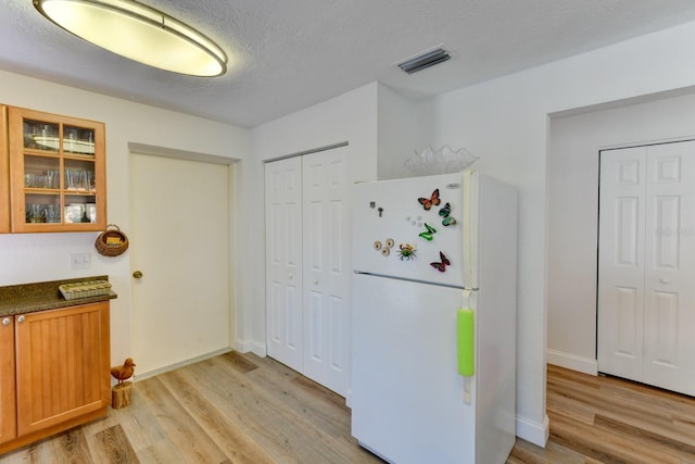 kitchen with a textured ceiling, white fridge, and light hardwood / wood-style floors