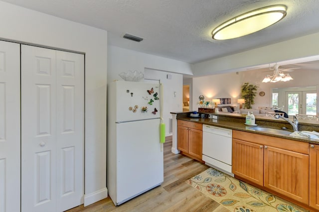 kitchen with sink, dark stone counters, a chandelier, white appliances, and light wood-type flooring