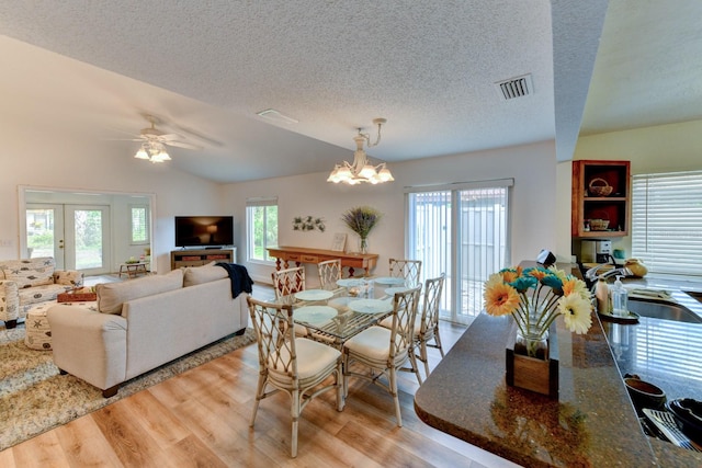 dining area featuring ceiling fan with notable chandelier, a textured ceiling, vaulted ceiling, sink, and light hardwood / wood-style flooring