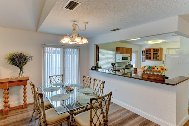 dining space with a notable chandelier, light wood-type flooring, and a textured ceiling