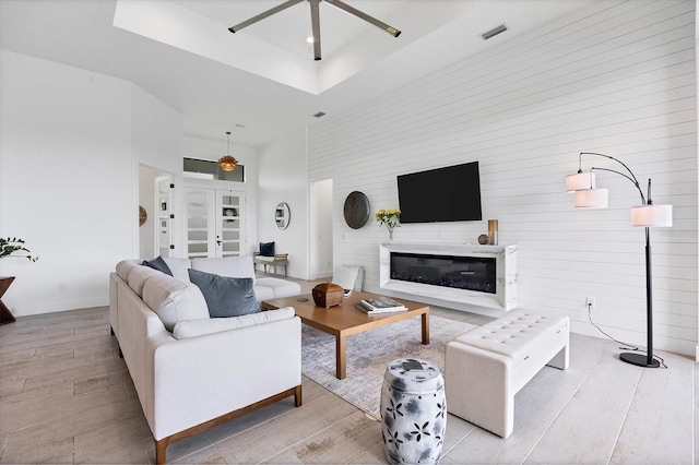 living room featuring ceiling fan, light hardwood / wood-style floors, a raised ceiling, and a high ceiling