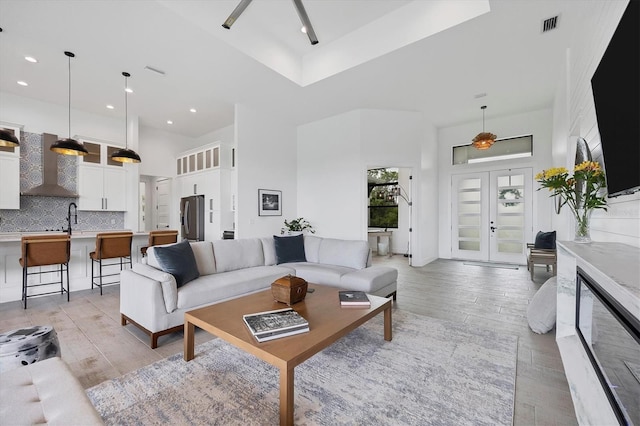 living room featuring sink, french doors, a high ceiling, and light hardwood / wood-style flooring