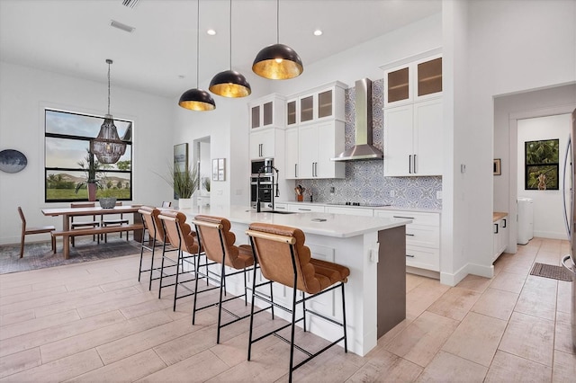 kitchen featuring decorative backsplash, white cabinetry, wall chimney exhaust hood, and hanging light fixtures