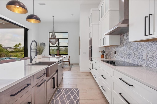 kitchen featuring white cabinetry, wall chimney exhaust hood, stainless steel appliances, pendant lighting, and decorative backsplash