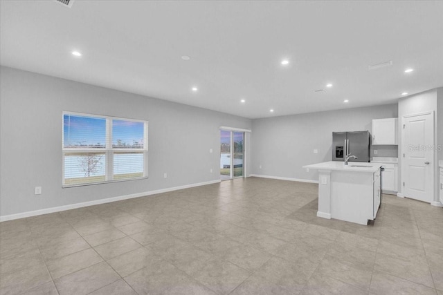 kitchen featuring light tile patterned floors, a center island with sink, stainless steel fridge, white cabinets, and sink