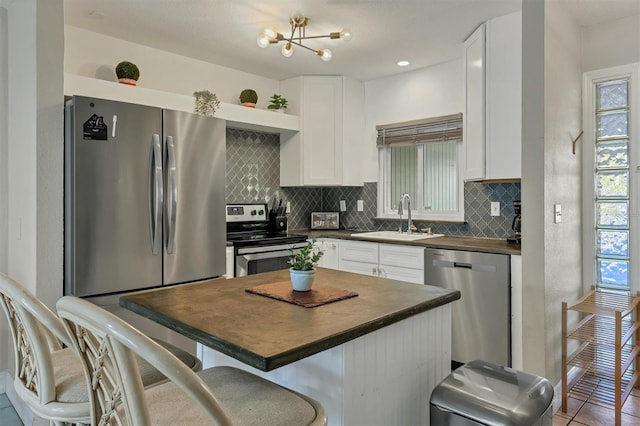 kitchen with decorative backsplash, stainless steel appliances, sink, white cabinets, and a chandelier