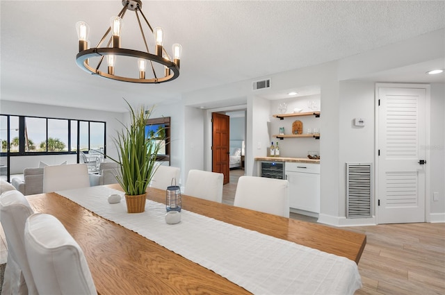 dining room featuring a notable chandelier, a textured ceiling, wine cooler, and light hardwood / wood-style flooring