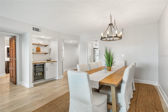 dining room featuring light hardwood / wood-style floors, indoor bar, wine cooler, and a chandelier