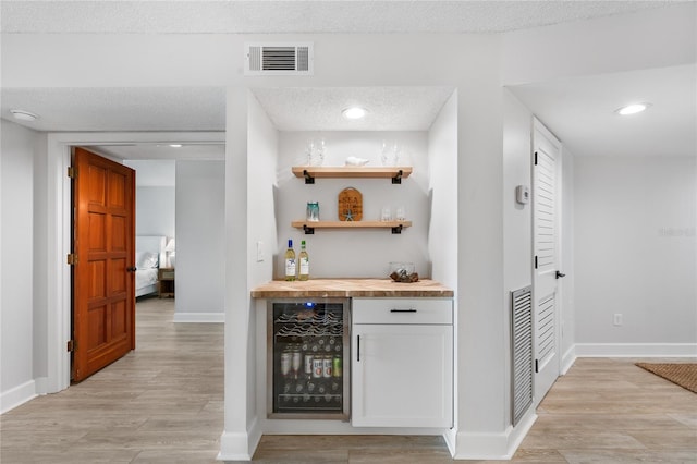 bar with wood counters, a textured ceiling, light wood-type flooring, and beverage cooler