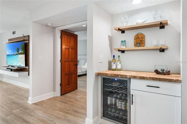 bar featuring wine cooler, a textured ceiling, butcher block countertops, light hardwood / wood-style floors, and white cabinetry