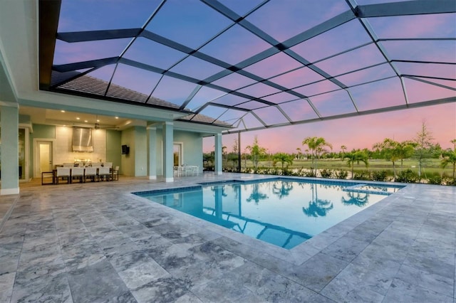 pool at dusk with glass enclosure, ceiling fan, and a patio area