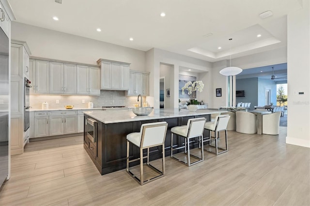 kitchen with stainless steel microwave, a kitchen breakfast bar, light stone countertops, a tray ceiling, and a large island