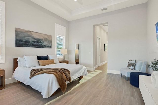 bedroom featuring ceiling fan, a raised ceiling, and light wood-type flooring